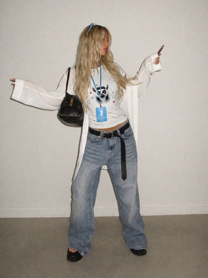 Person wearing a white coat, blue jeans, and holding a black bag against a plain background
