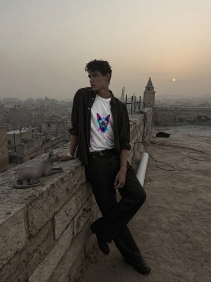 Person wearing a white t-shirt with a colorful graphic design, standing on a rooftop with a cityscape in the background.