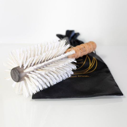 Glass cleaning brush with white bristles and cork handle on a black cloth with gold text.