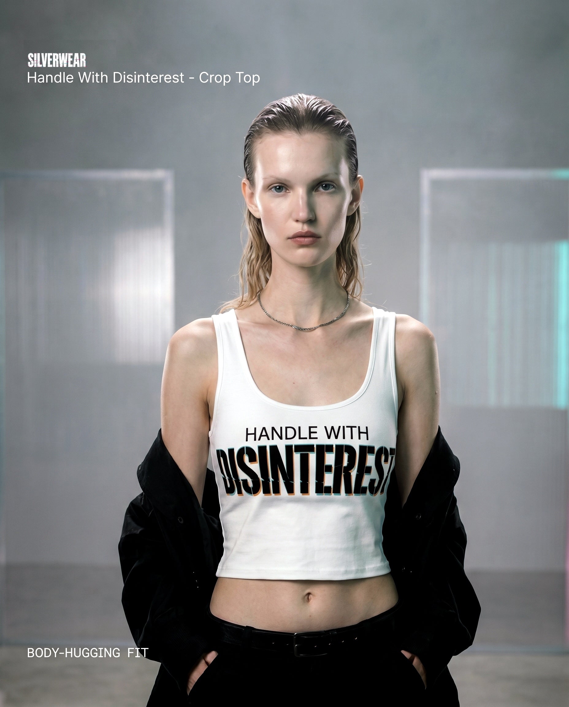 Woman wearing a white crop top with 'Handle With Disinterest' text, standing in a modern indoor setting.
