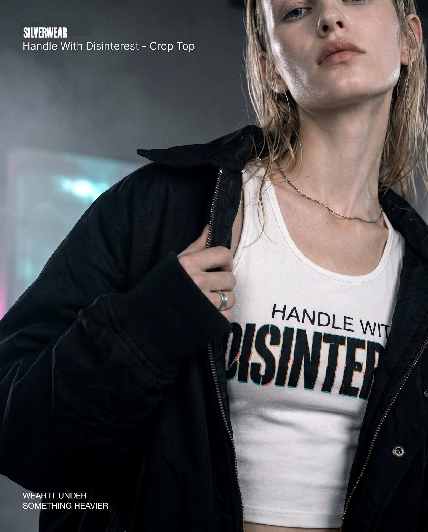 Woman wearing a white crop top with 'Handle With Disinterest' text, holding a black jacket.