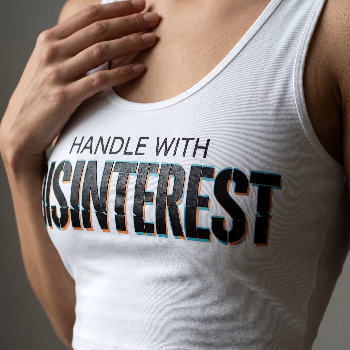 Person wearing a white tank top with text 'HANDLE WITH DISINTEREST' on a gray background