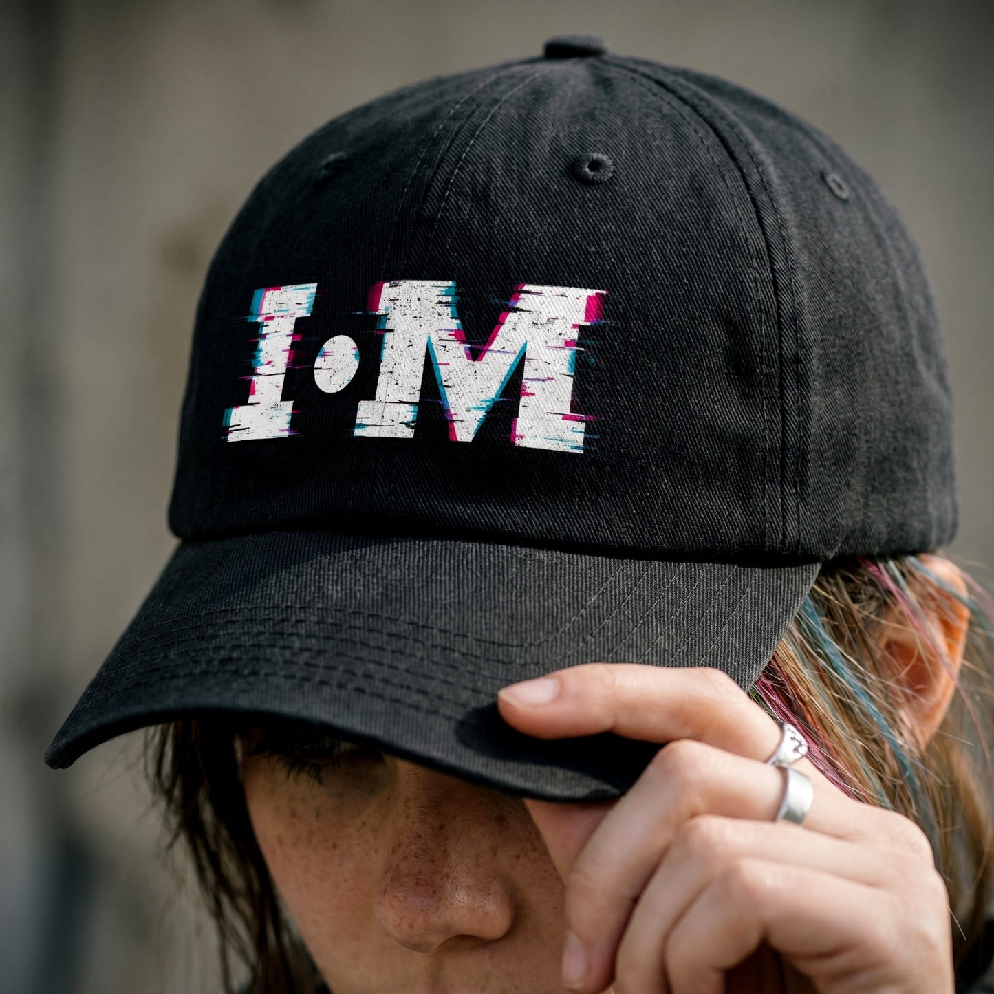Black cap with 'I·M' text worn by a person against a neutral background