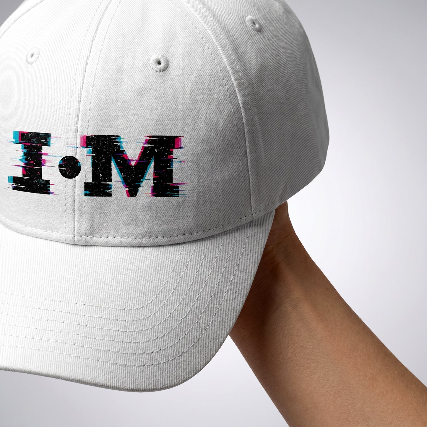 White cap with 'I·M' logo held by a person against a white background