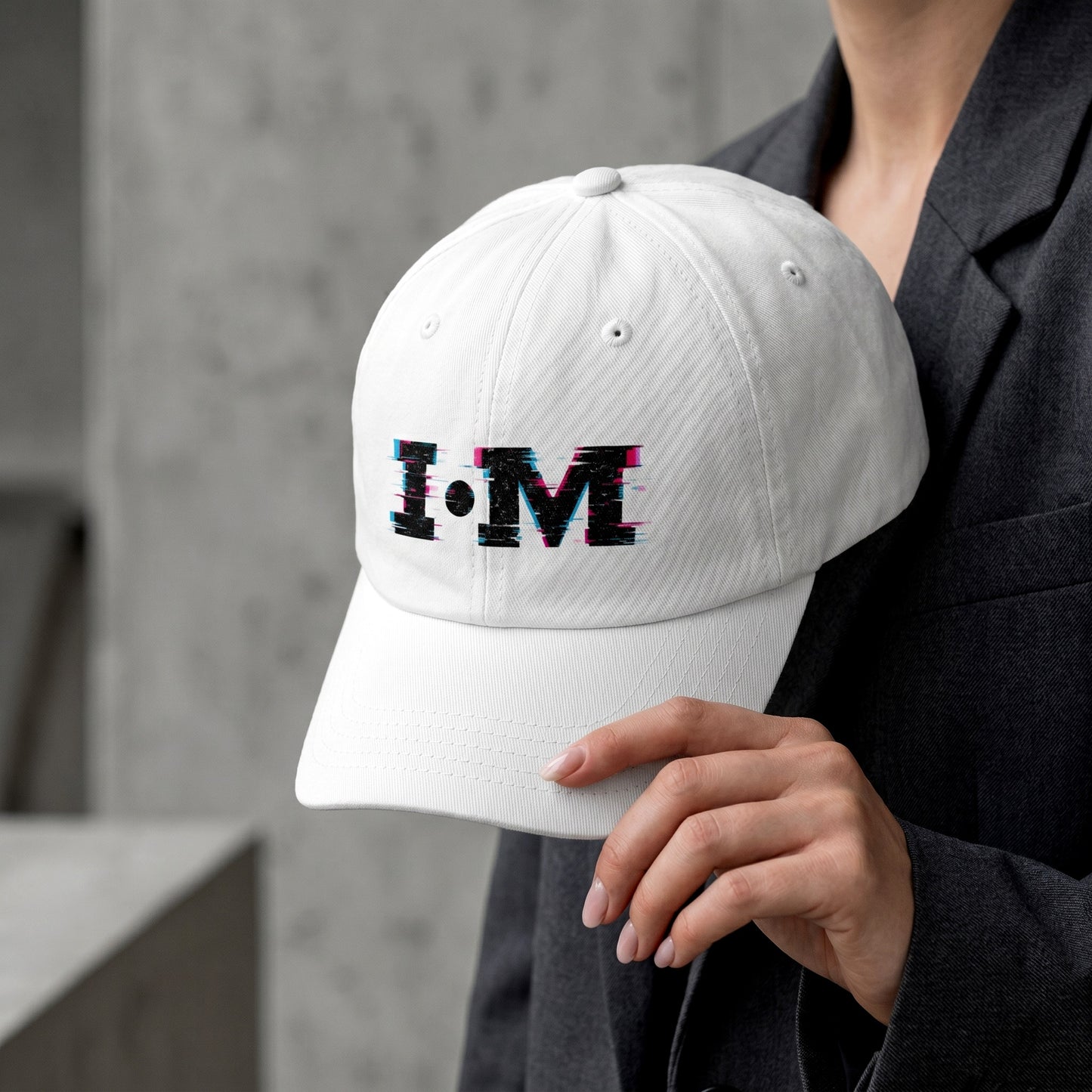 White cap with colorful 'I AM' text held by a person against a concrete wall.