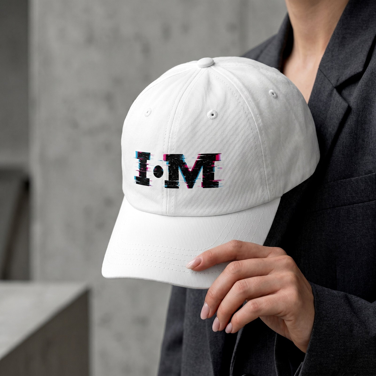 White cap with colorful 'I AM' text held by a person against a concrete wall.