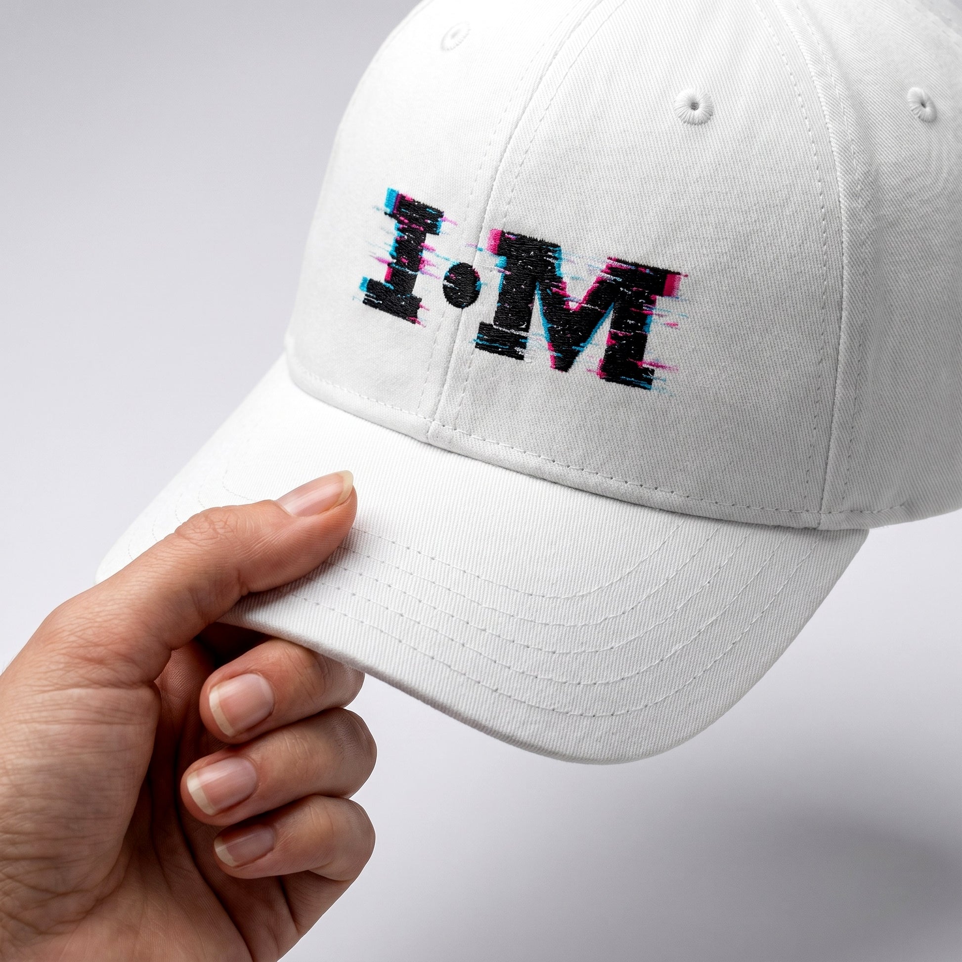 White cap with 'I.M' text held by a hand on a light gray background