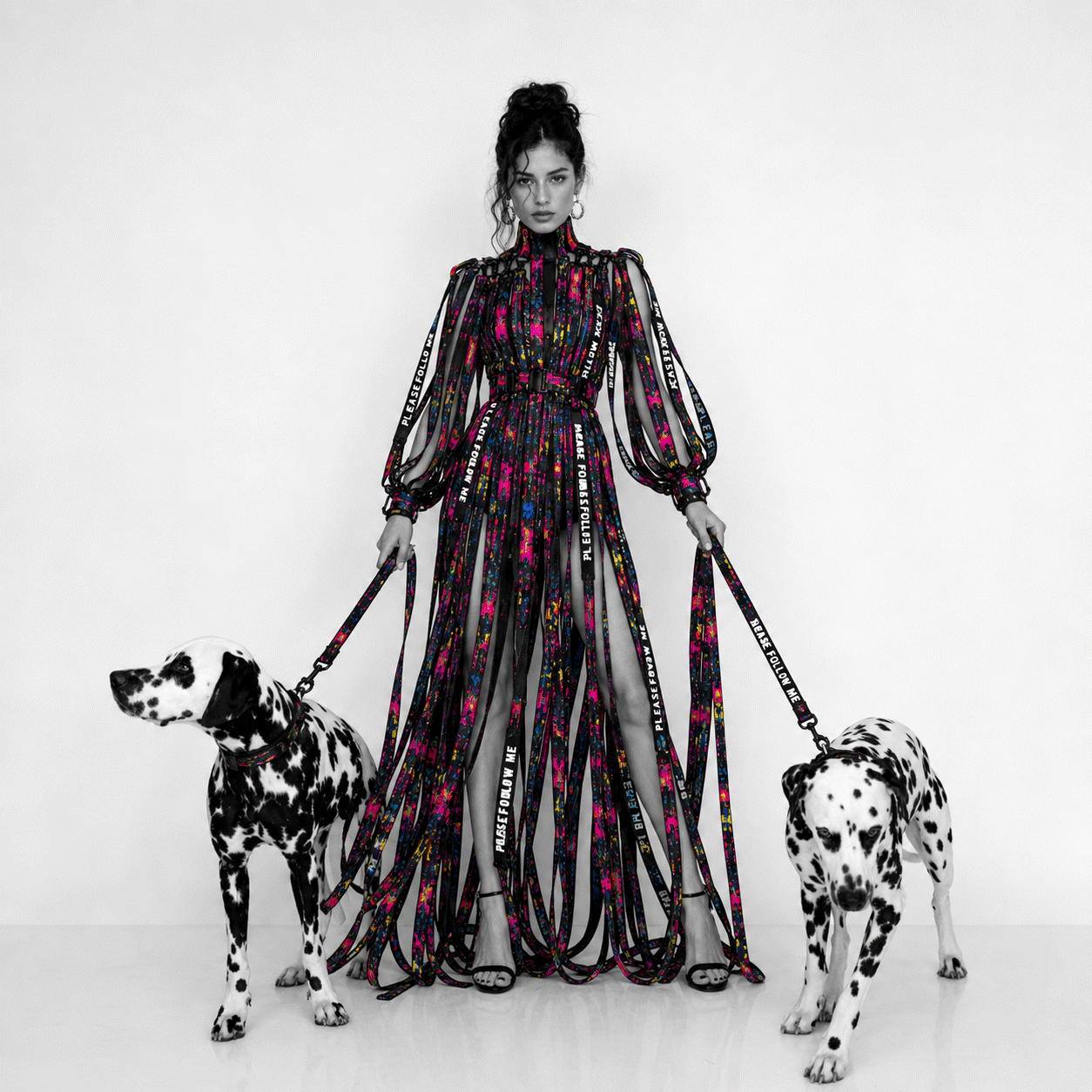 Woman in a colorful dress with two Dalmatian dogs on leashes against a white background