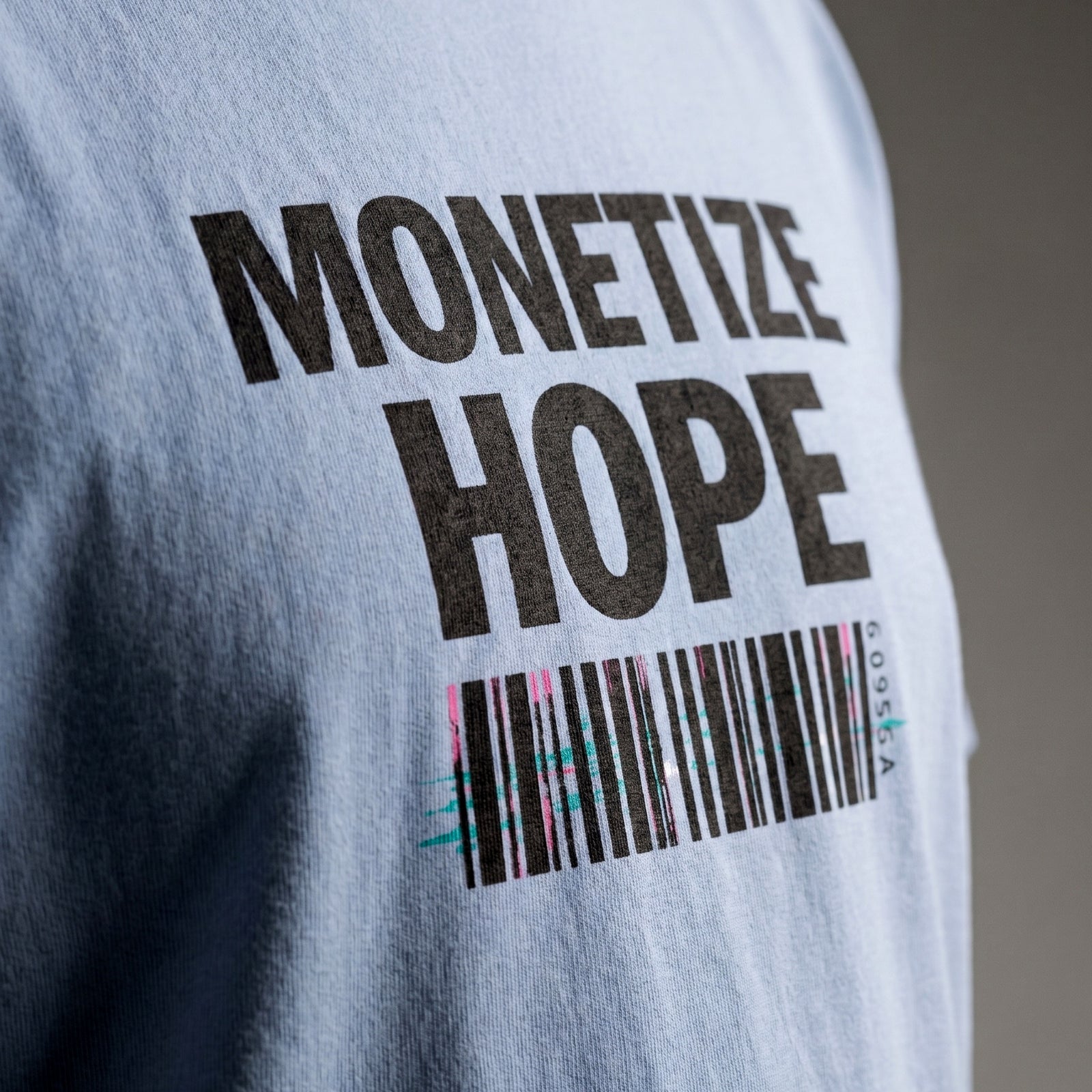 Gray t-shirt with 'MONETIZE HOPE' text and barcode design on a blurred background
