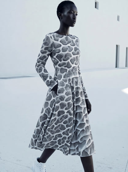 Editorial fashion image of a model wearing the ANSO Cellular Mesh Midi Dress against a warm neutral studio background, showing the long sleeves, flared midi skirt, and sculptural grey mesh print.