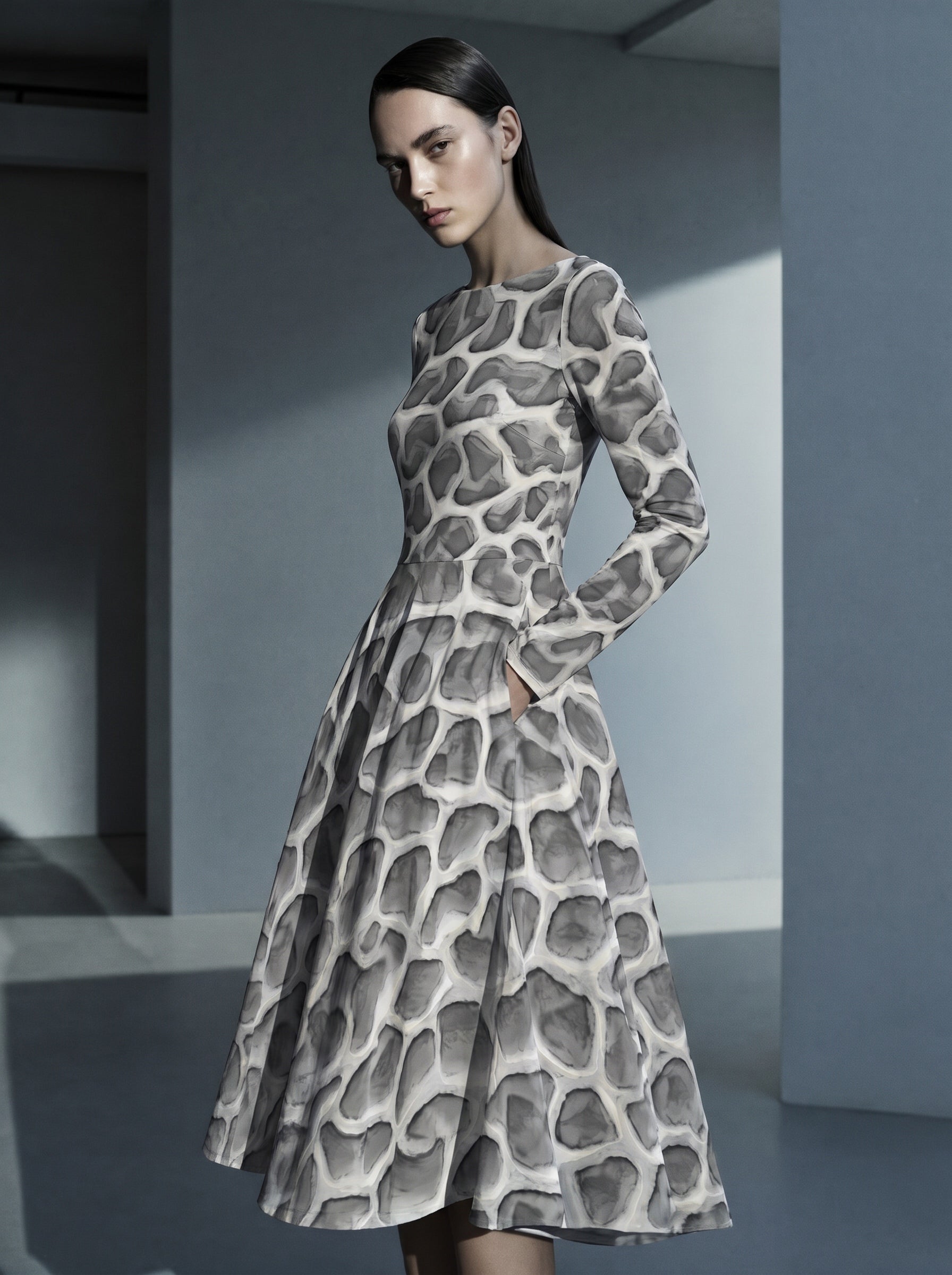 High-end editorial image of a model wearing the ANSO Cellular Mesh Midi Dress in a cool-toned architectural interior, highlighting the fitted waist, long sleeves, side pocket, and flared skirt.