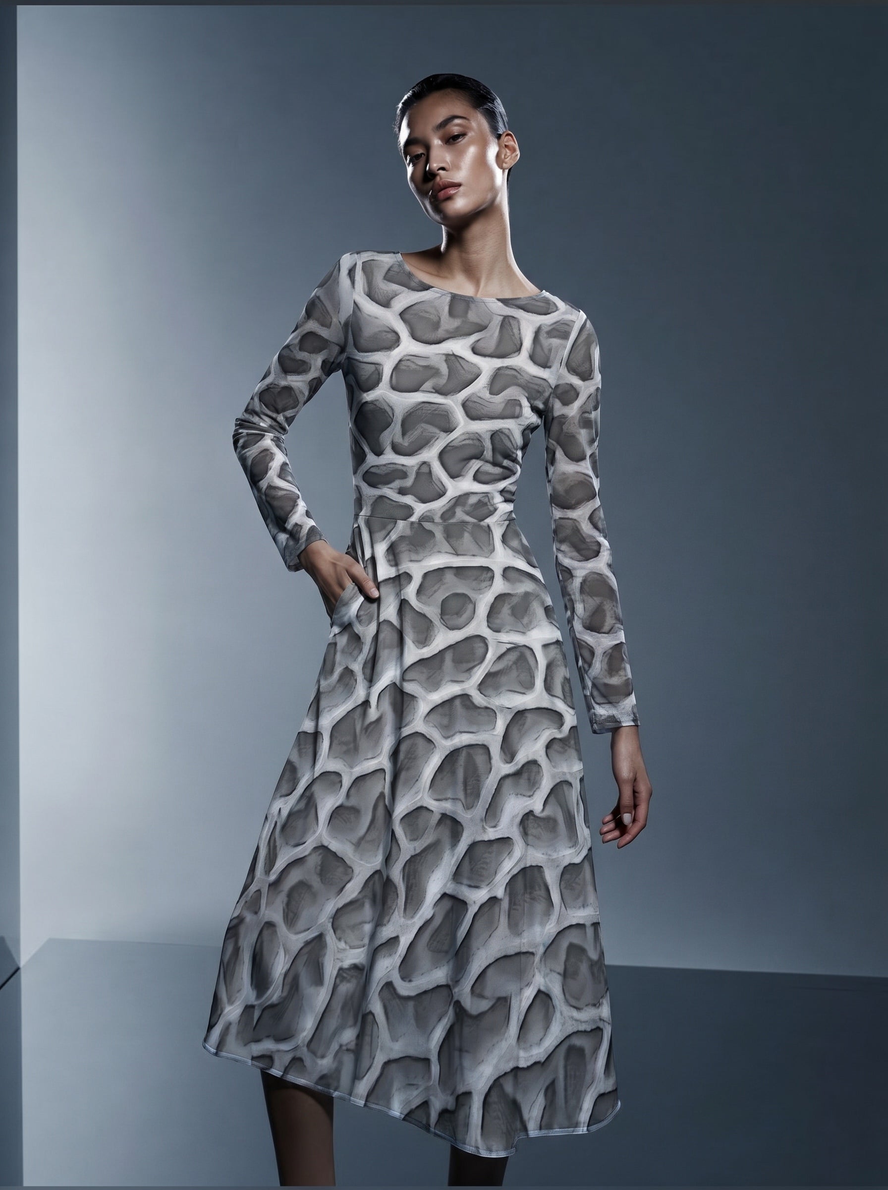 Editorial studio portrait of a model wearing the ANSO Cellular Mesh Midi Dress against a blue-grey background, showing the fitted upper body, long sleeves, side pocket, and midi-length flared skirt.