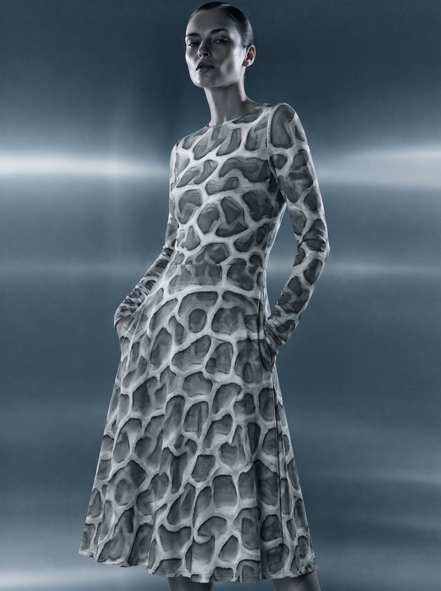 Model wearing the ANSO Cellular Mesh Midi Dress in a cinematic blue-grey studio setting with horizontal light bands, highlighting the dress silhouette, pocket detail, and all-over cellular mesh print.