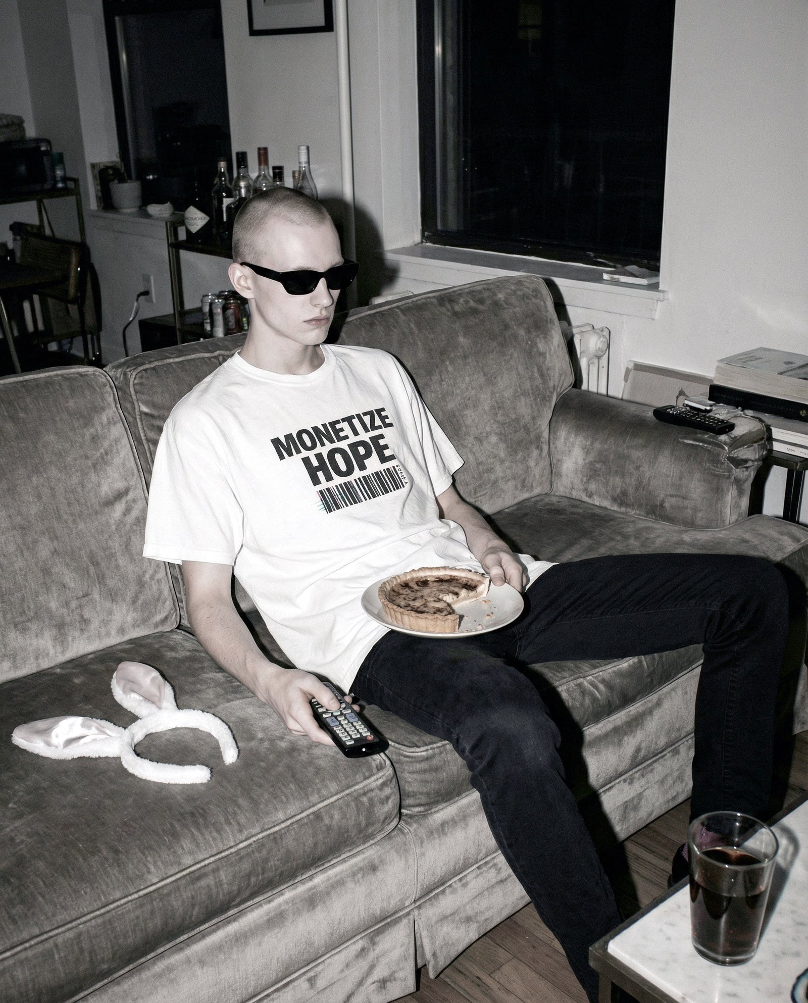 Person sitting on a couch wearing a t-shirt with 'Monetize Hope' text, holding a plate with food.