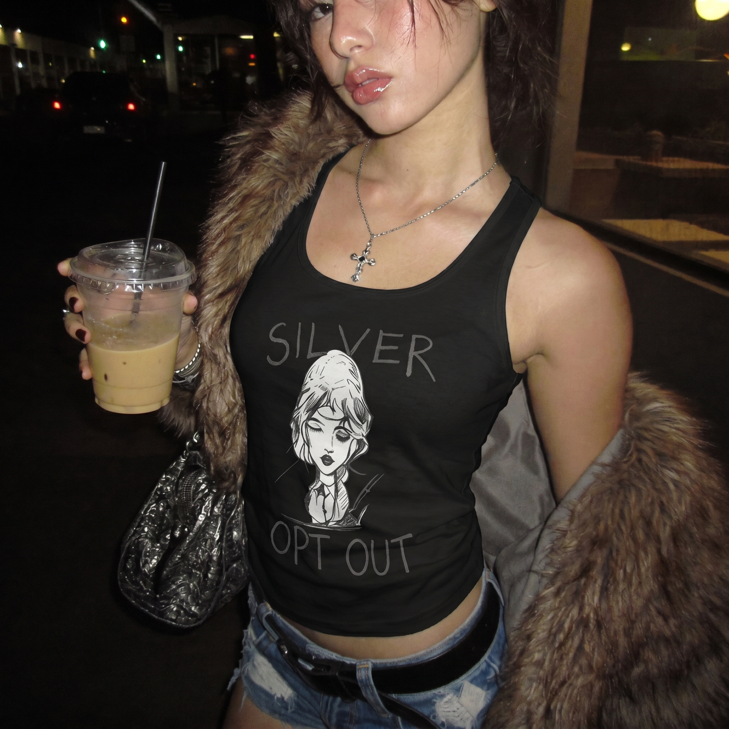 Woman wearing a black tank top with 'SILVER OPT OUT' text and graphic, holding a drink at night.