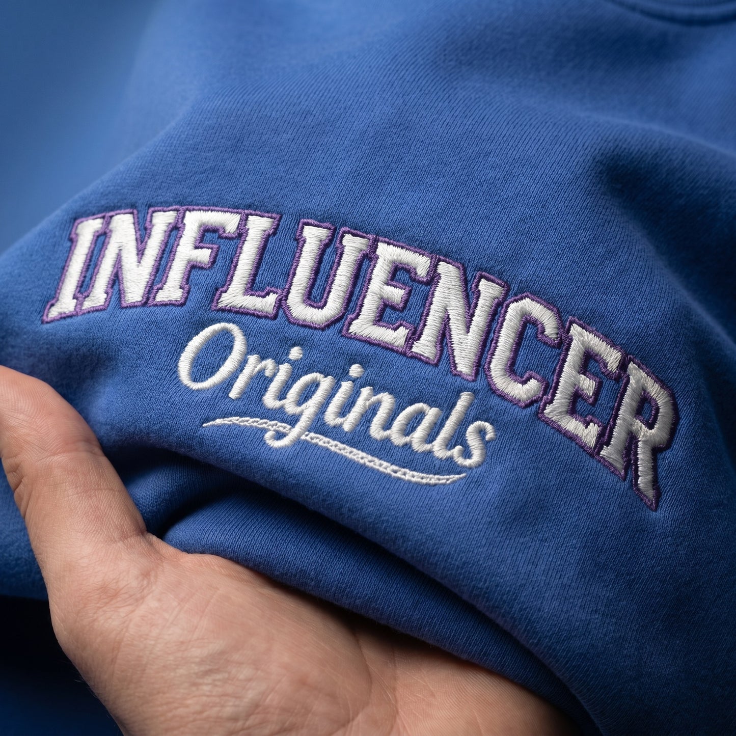 Blue fabric with 'INFLUENCER Originals' embroidered on it, held by a hand.